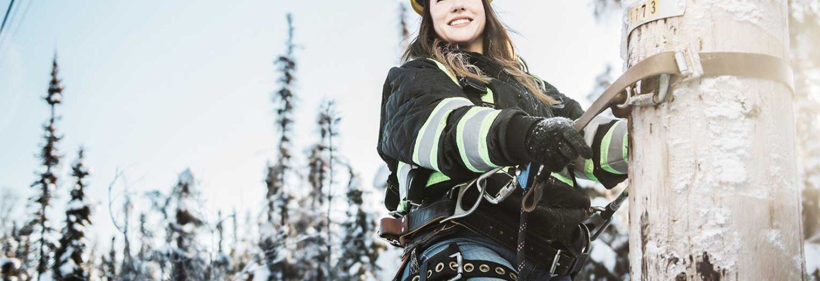 Service technician Nicole climbing a pole in a snowed northern background