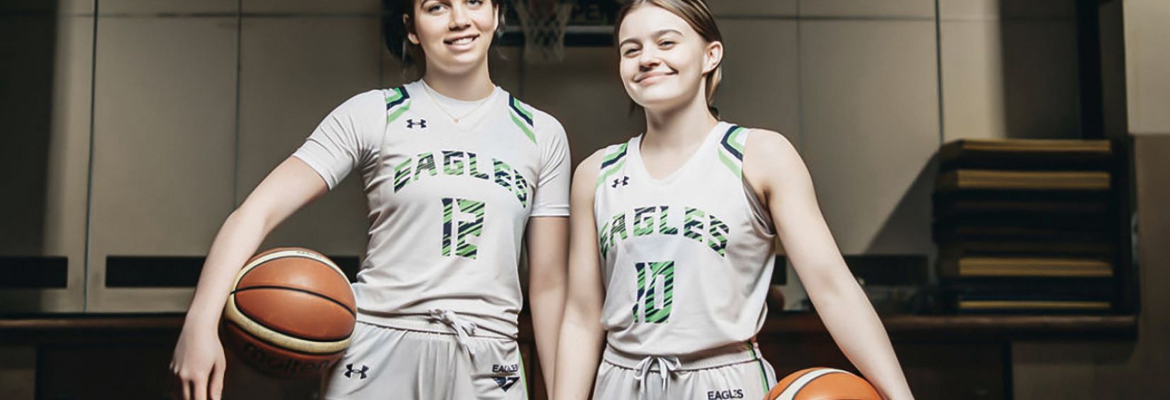 Lilly and Grace stand on the court, basketball in their hands, smiling brightly.